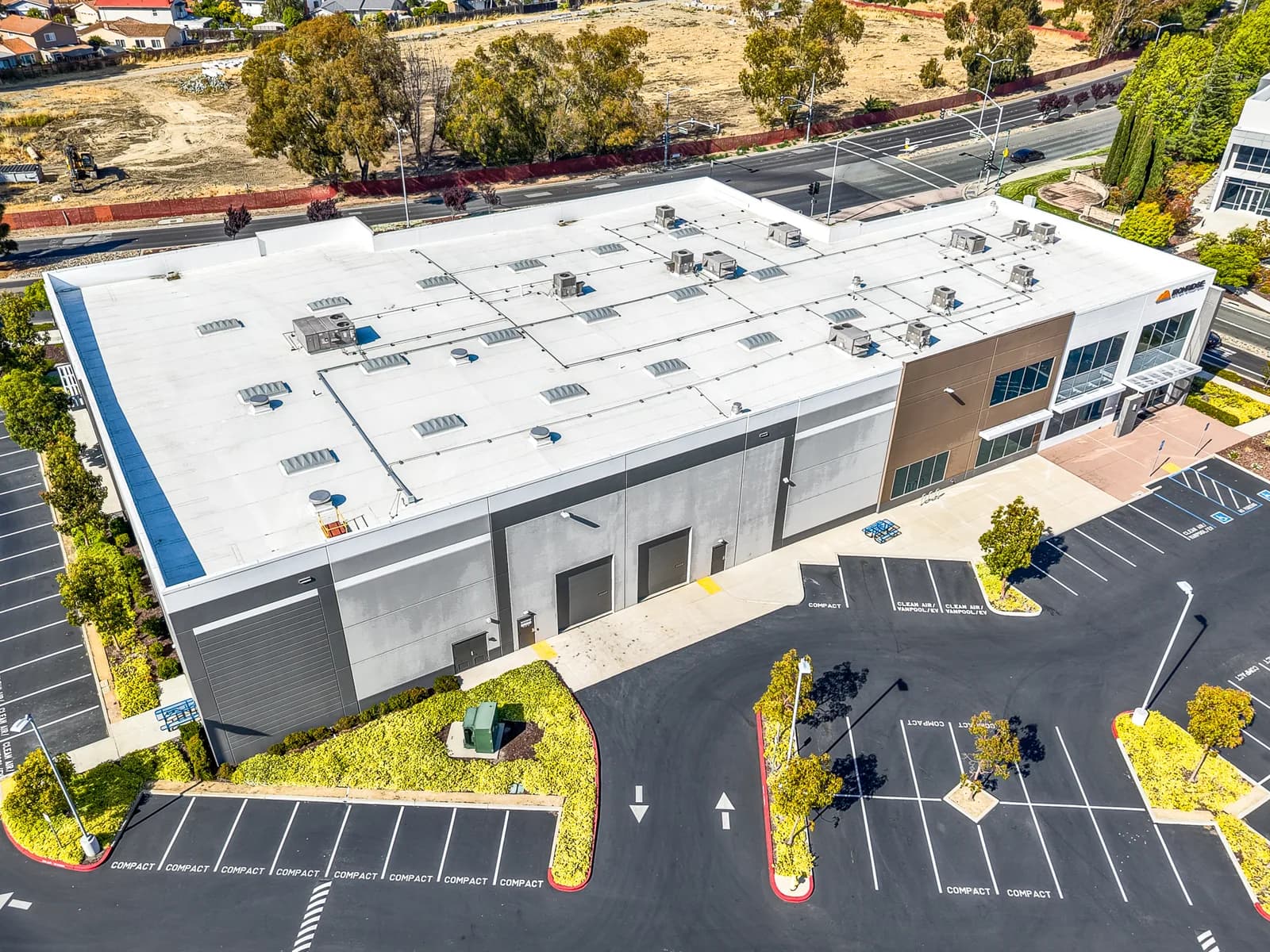 Aerial view of a large commercial building with a white roof and HVAC units, surrounded by a parking lot