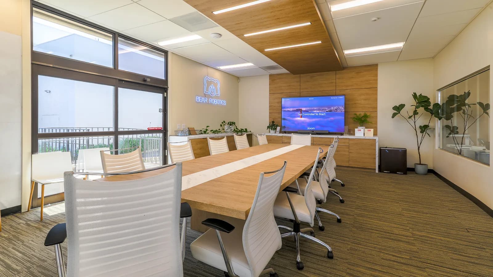 Conference room with long wooden table, white chairs, neon Bear Robotics logo, and a mounted TV