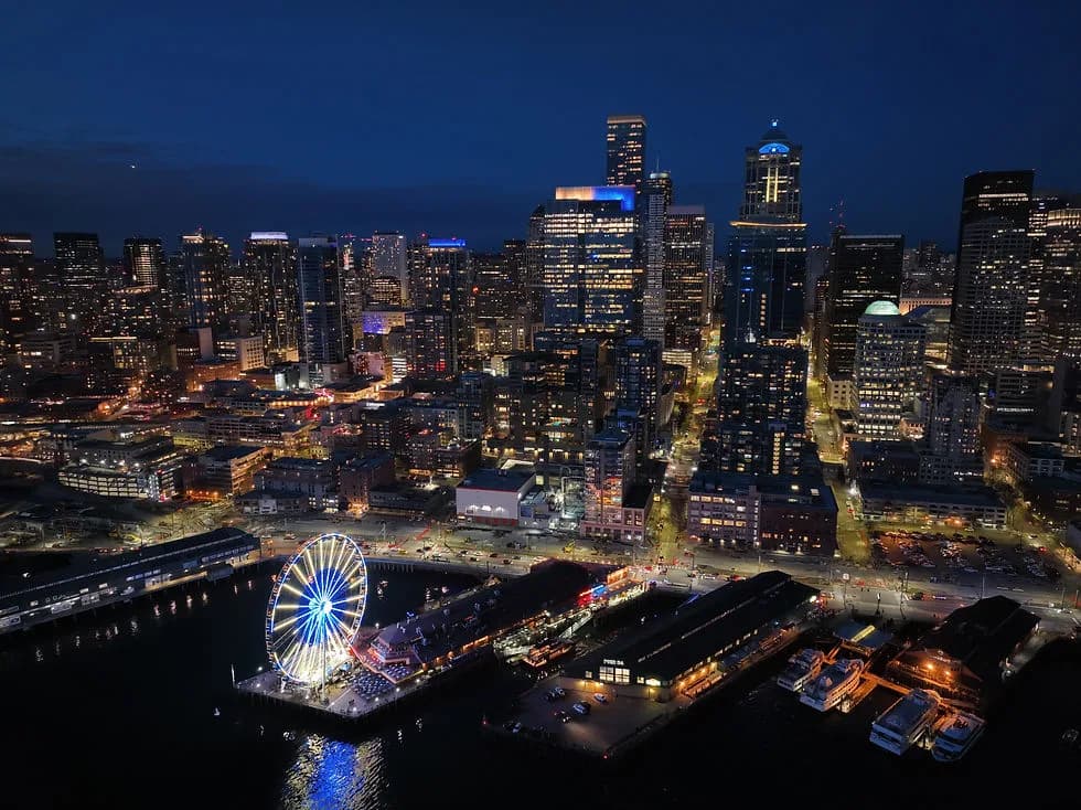 Nighttime city skyline along the harbor with a lit ferris wheel on a pier and boats