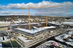 Aerial view of a construction site with a partially built building and two yellow cranes near water
