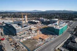 Aerial view of a large construction site with cranes, a green building, and surrounding roads