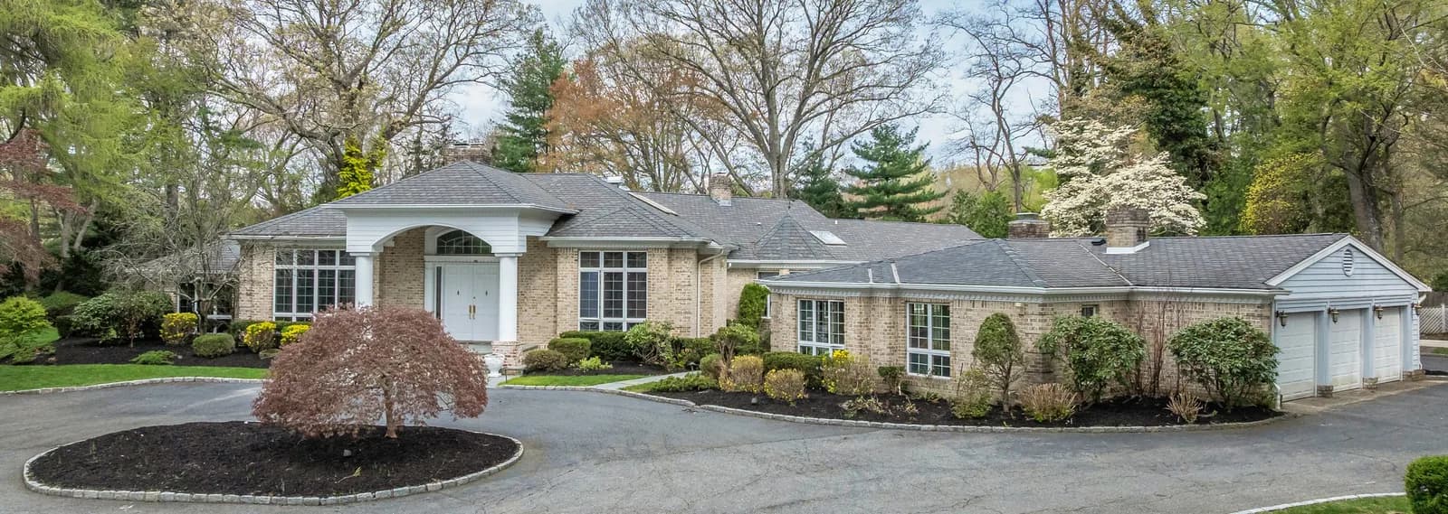 Brick single-story house with a circular driveway and a round island with a small tree, plus three-car garage