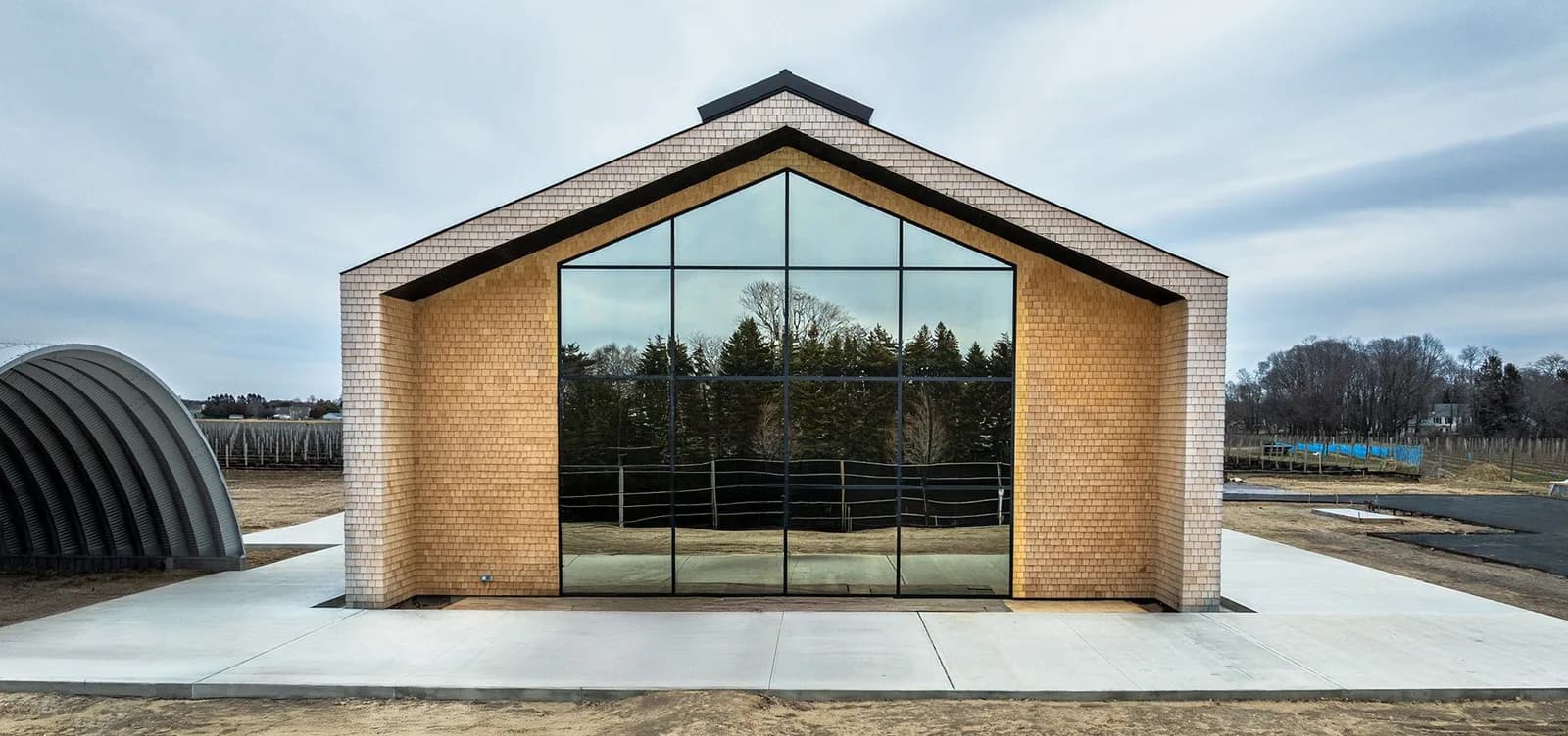 Brick building with a large glass front and triangular roof, trees reflected in the glass panels