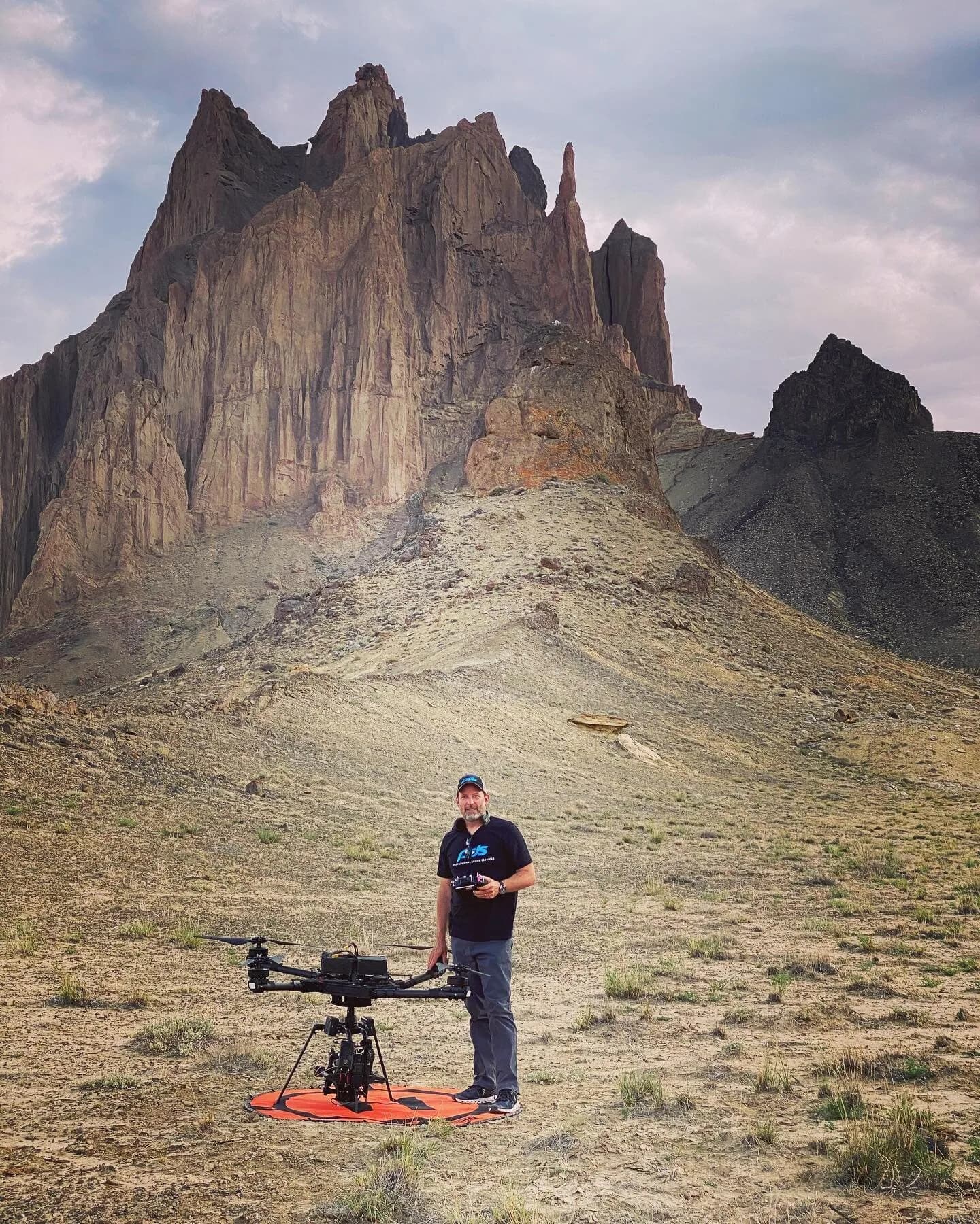 Man with drone on an orange landing pad in front of jagged rock cliffs