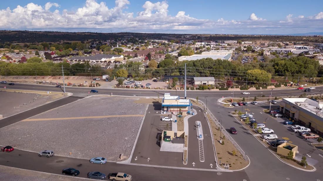 Aerial view of a suburban commercial area with a small drive-through, parking lots, and distant homes