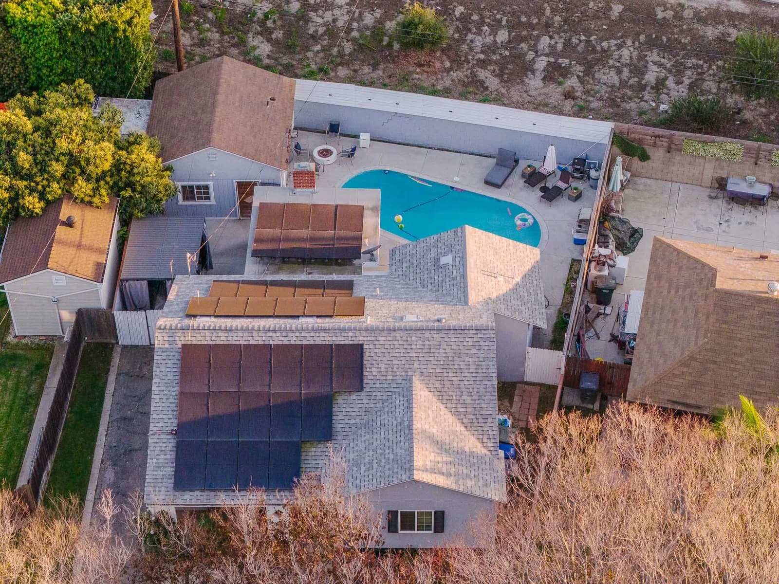 Aerial view of a backyard with a kidney-shaped blue pool, lounge chairs and patio area, surrounded by houses