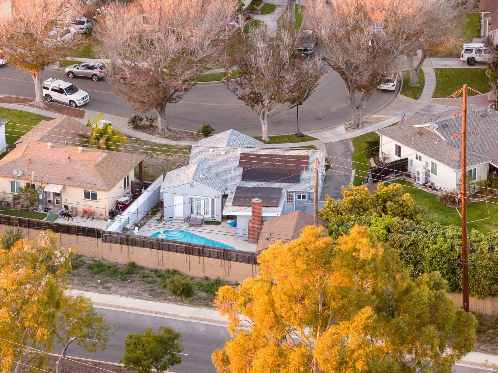 Aerial view of a suburban neighborhood with houses, solar panels on roofs, and a backyard pool