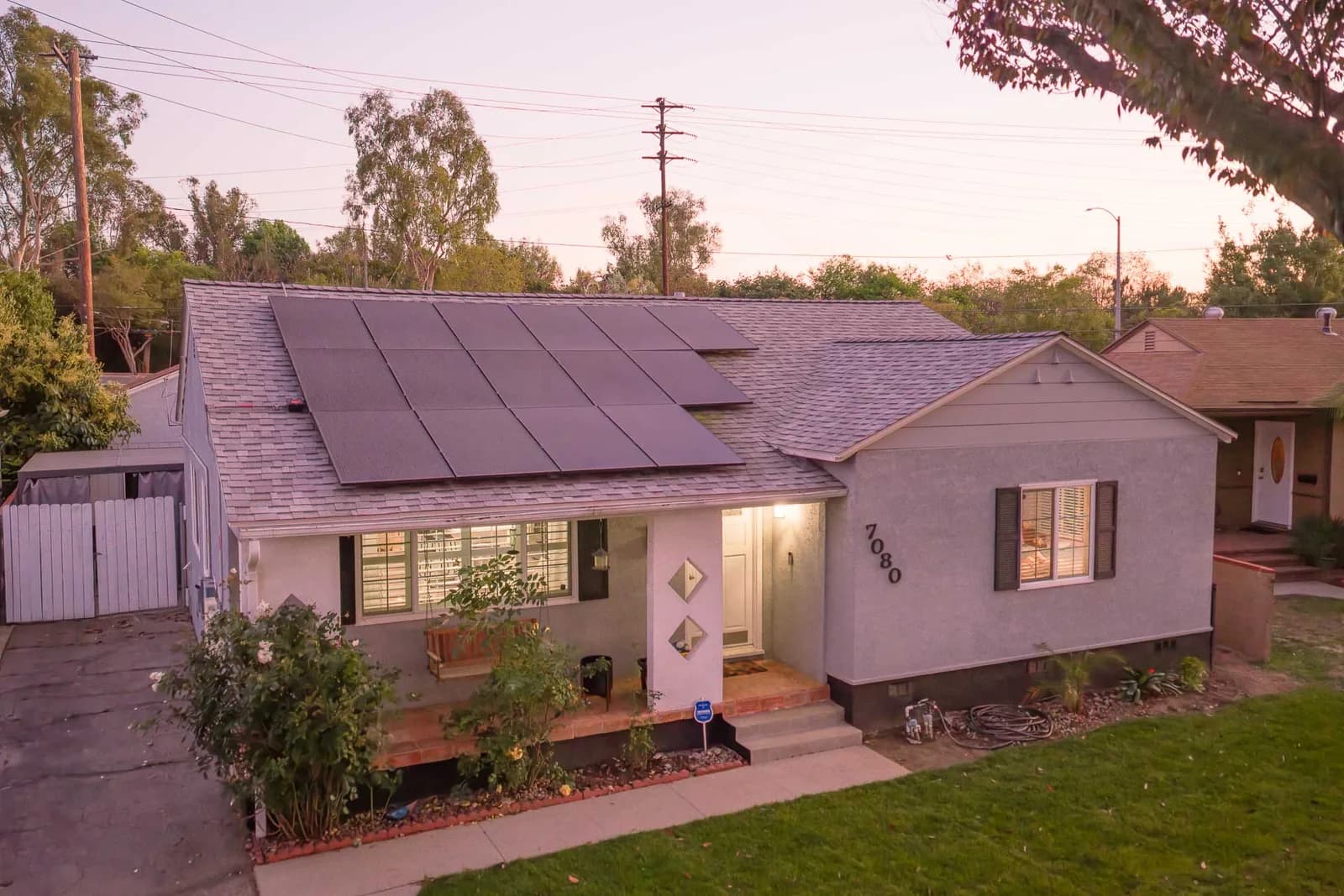 Aerial view of a gray single-story house with solar panels on the roof, a front yard and driveway