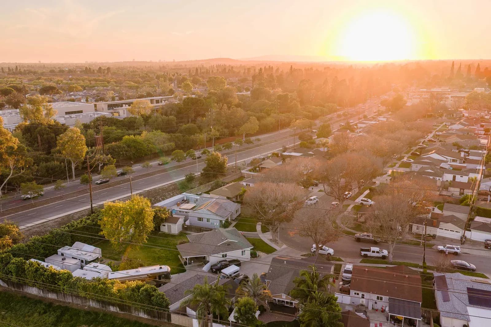 Aerial view of a suburban neighborhood at sunset with trees, houses, and power lines