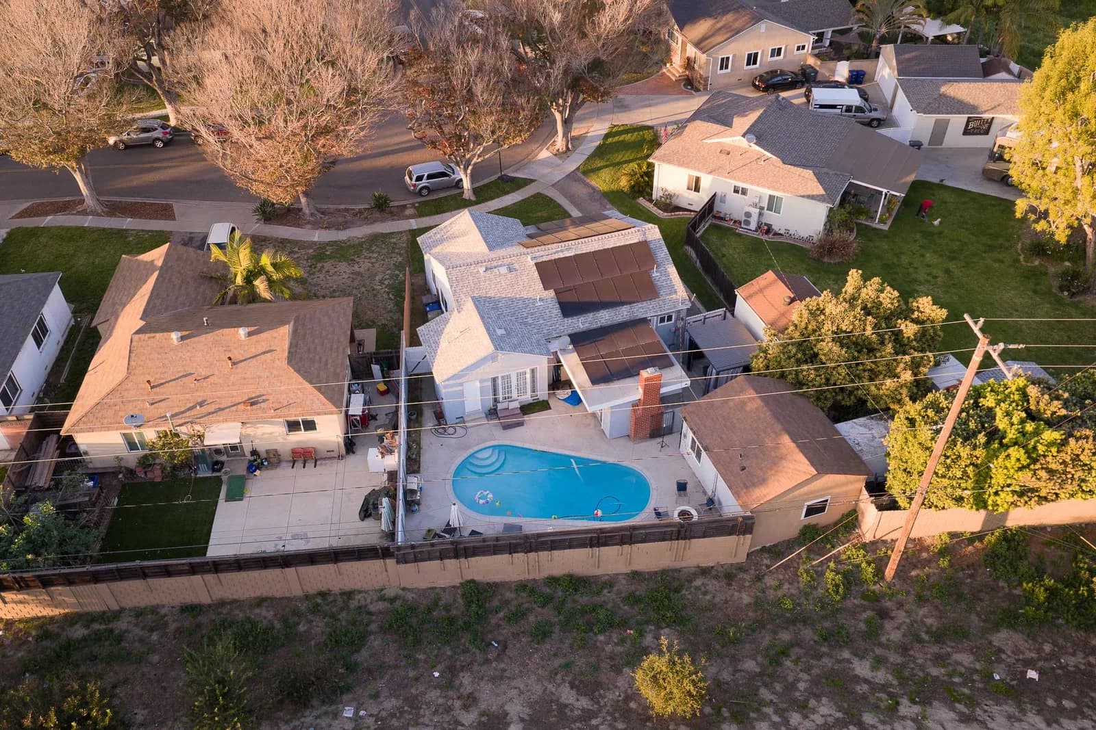 Aerial view of a suburban neighborhood with a central house, a kidney-shaped pool, and solar panels on roofs