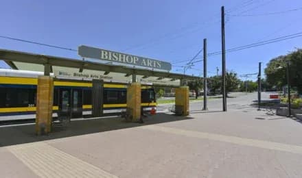 Platform at Bishop Arts Station with a yellow train, canopy, and power lines