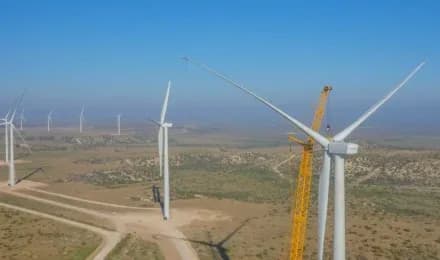 Aerial view of wind turbines in a desert landscape, with a yellow crane beside a turbine