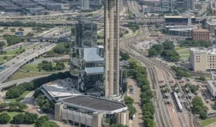 Industrial facility with a tall smokestack, a glass building, and nearby rail tracks