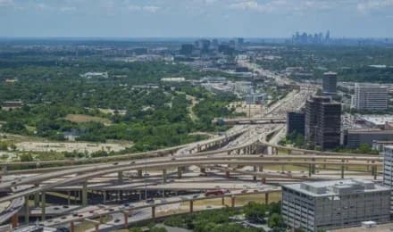 Aerial view of a multi level highway interchange with overpasses, green spaces, and distant city skyline