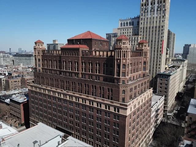Aerial view of a large brown brick building with red-roofed corner towers in a city