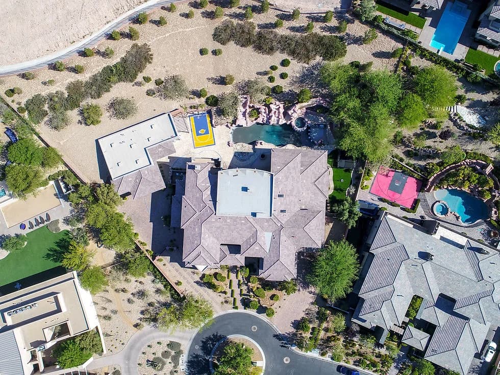 Aerial view of a large multi-wing house with a circular driveway, a pool area, and desert landscaping