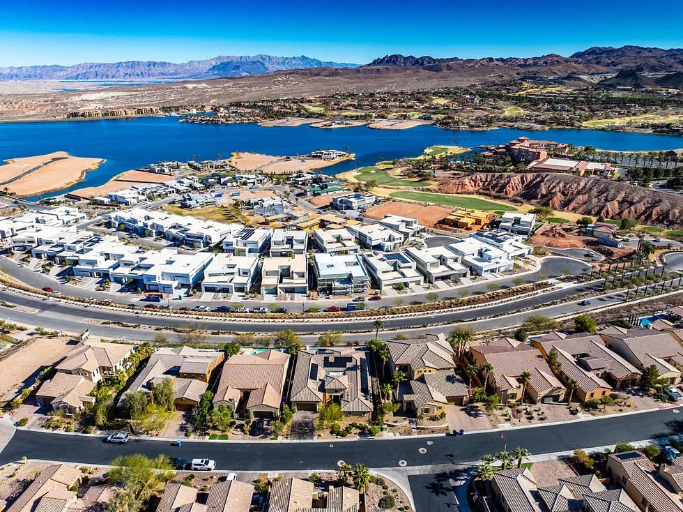 Aerial view of a suburban housing development along a blue lake, with mountains in the distance