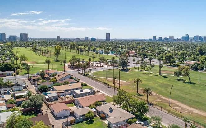 Oblique aerial view of houses beside a golf course with distant city skyline