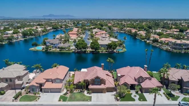 Aerial view of suburban waterfront homes lining a curved lake under a clear blue sky