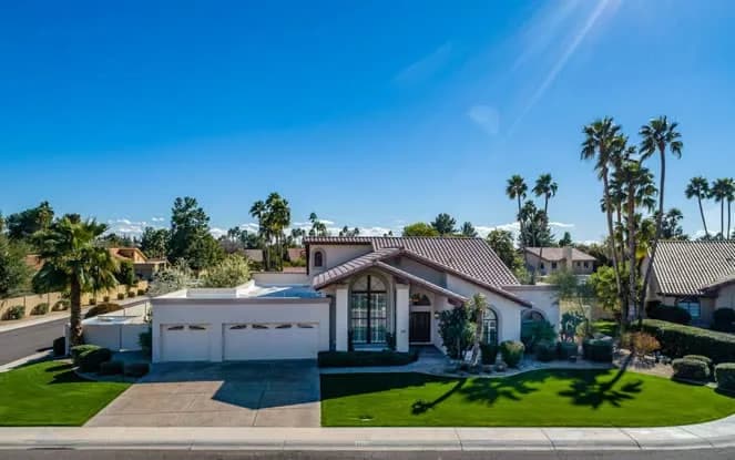 Suburban single-story house with tile roof, green lawn and palm trees photographed from above