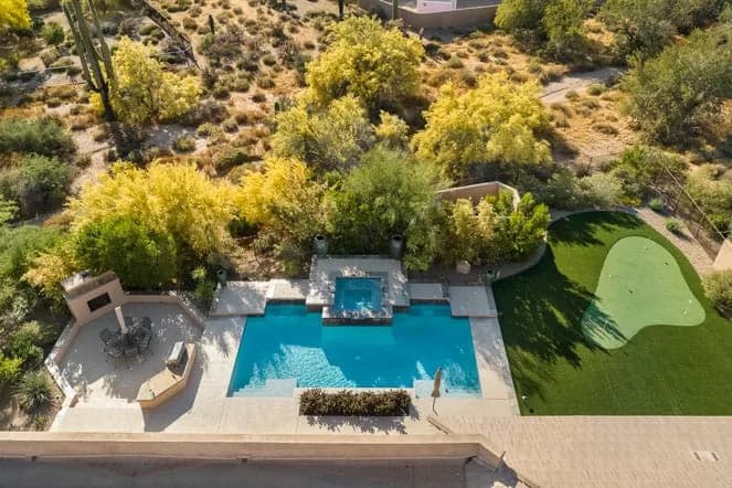 Aerial view of a backyard with rectangular pool, spa, patio dining area and small putting green