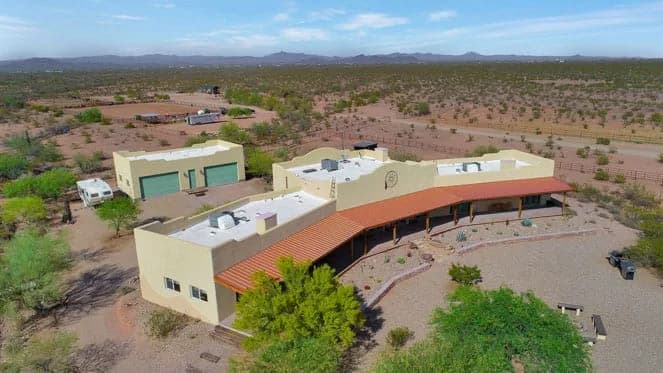 Aerial view of a southwestern single-story home with curved covered porch, detached garage, and desert landscape