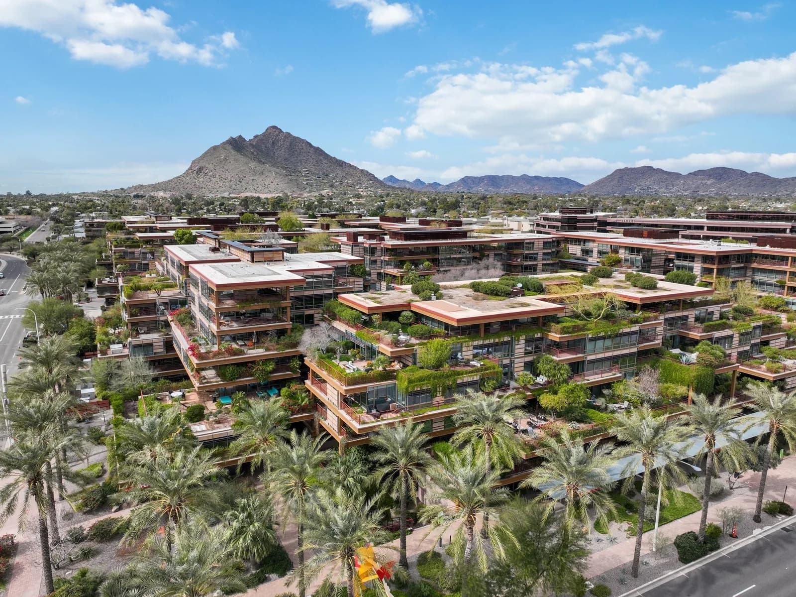 Aerial view of terraced office buildings with rooftop gardens, palm trees and distant mountains