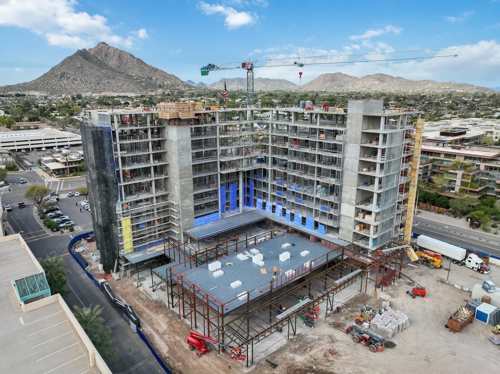 Aerial view of a multi-story building under construction with crane and surrounding mountains