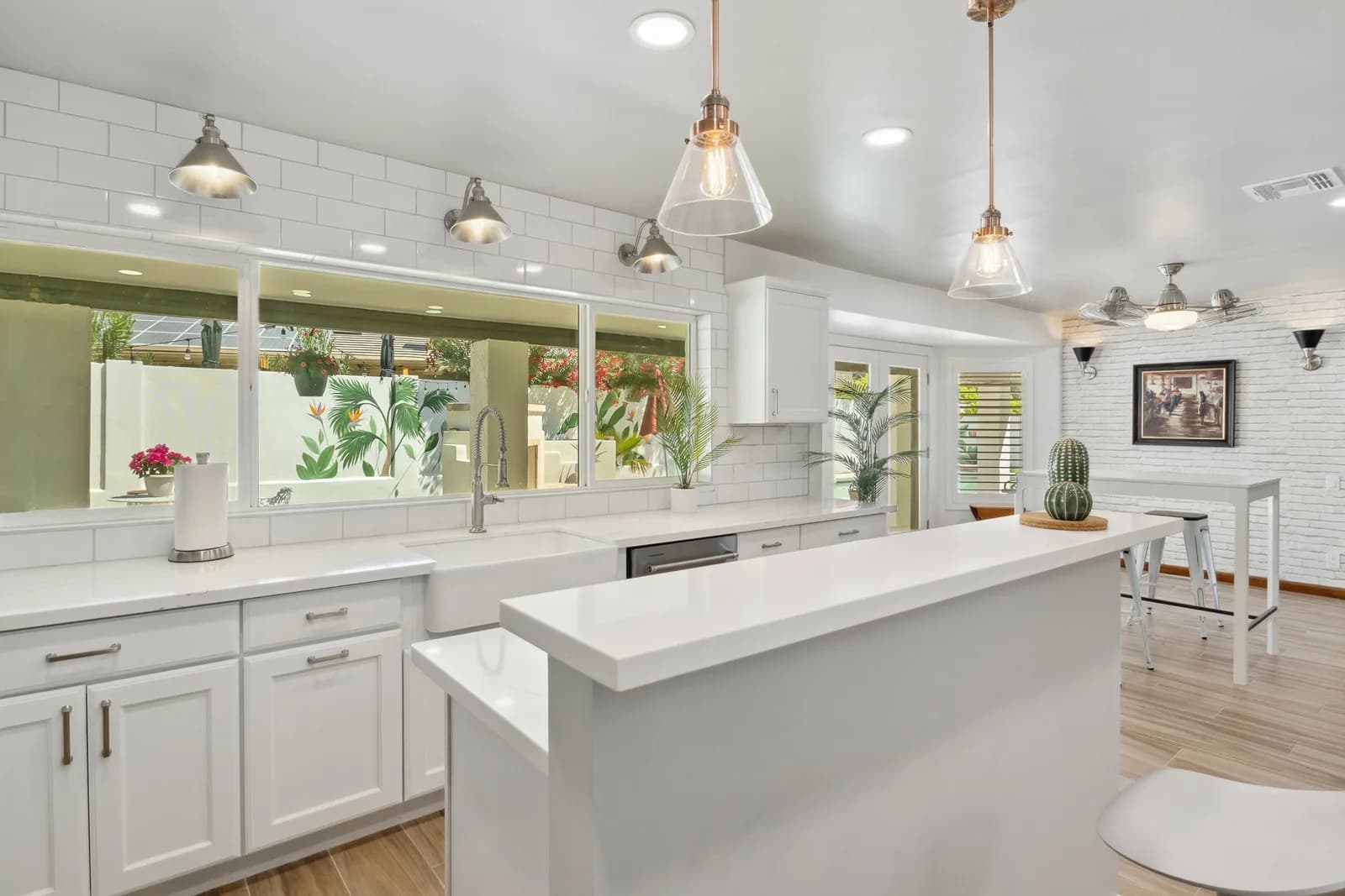 Bright white modern kitchen with breakfast island, pendant lights, farmhouse sink and potted plants