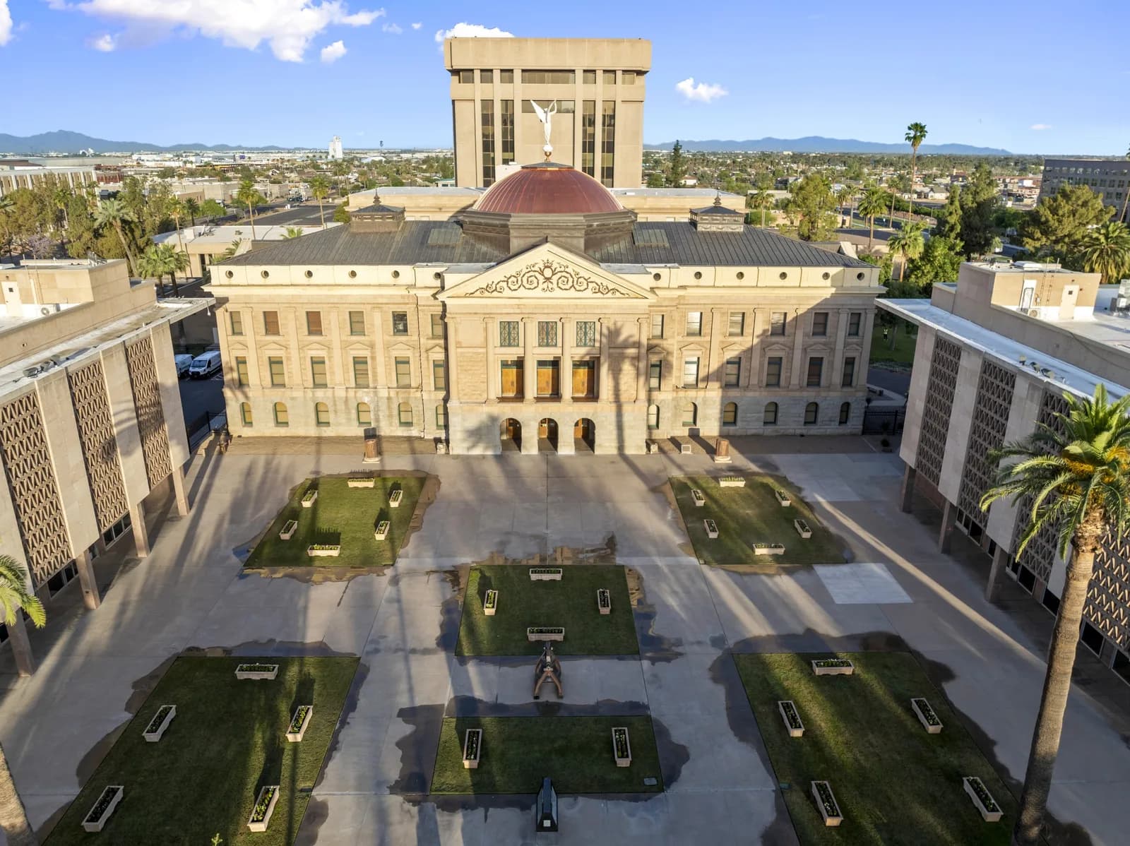 Aerial view of a classical courthouse with a central dome, courtyard lawns, planters and long palm shadows