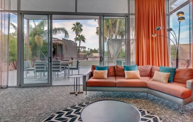 Bright mid-century living room with orange sectional, floor lamp and sliding glass doors to patio