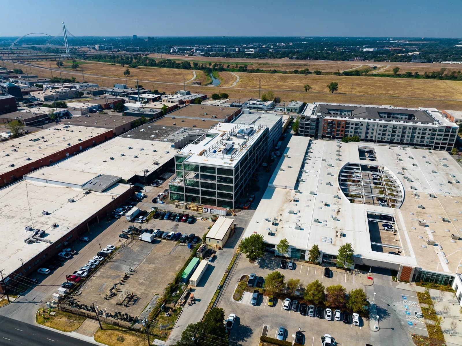 Aerial view of a commercial complex with flat rooftops, a glass-fronted building, and parking lots