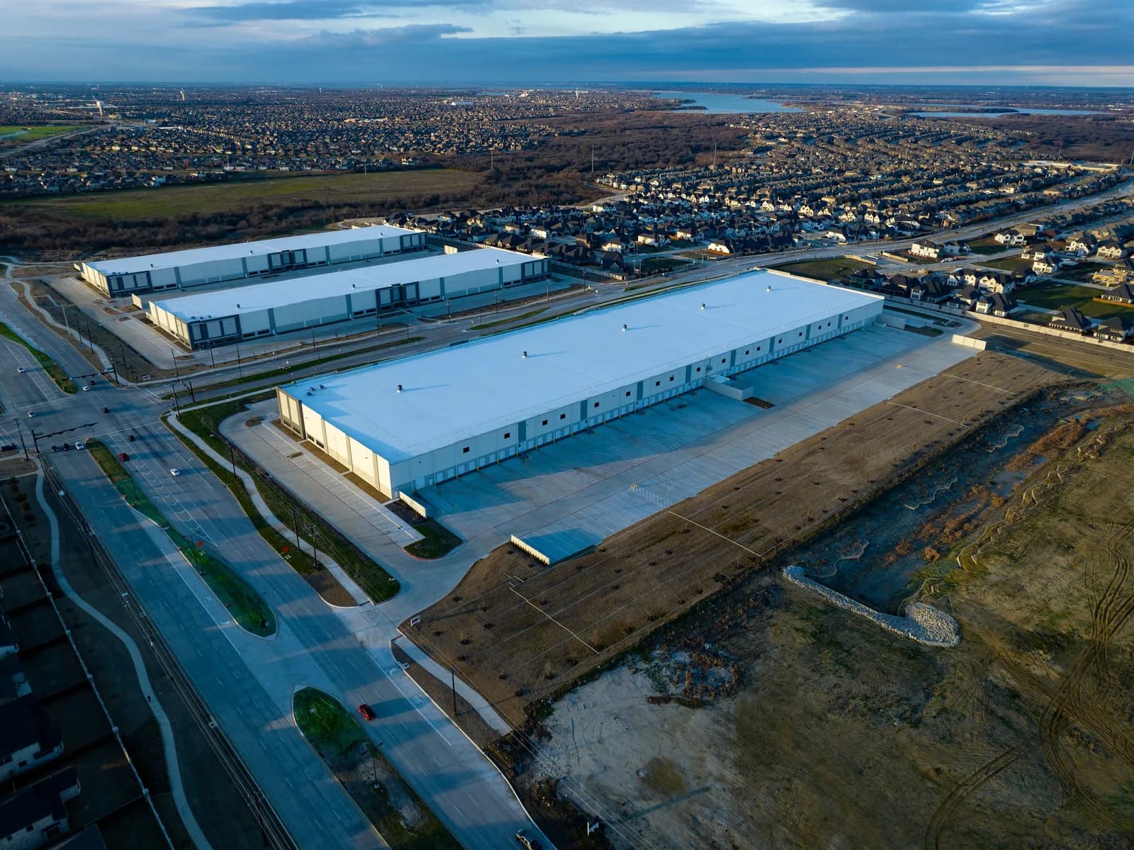 Aerial view of large white-roof industrial warehouses with surrounding roads and a residential suburb