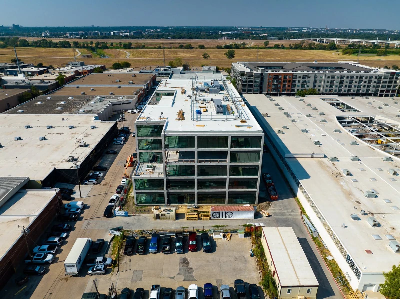 Drone view of a glass-fronted office building under construction, surrounded by blocks and parked cars