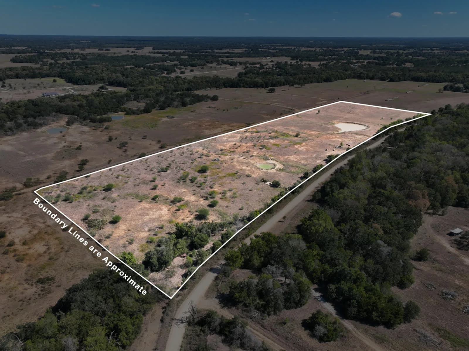 Aerial view of a rectangular parcel outlined in white, with dirt fields, trees, and a road along the edge