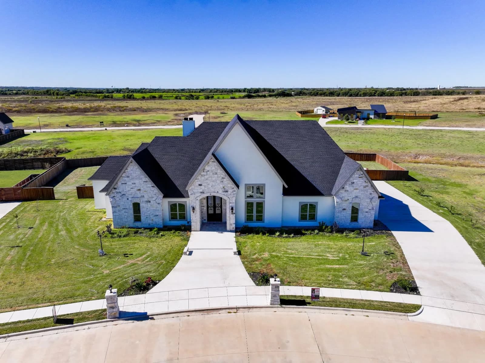 Aerial view of a large white stone house with a dark roof and arched entry