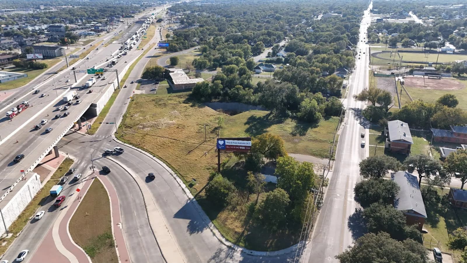 Aerial view of a highway interchange with an overpass, roundabout, and surrounding trees