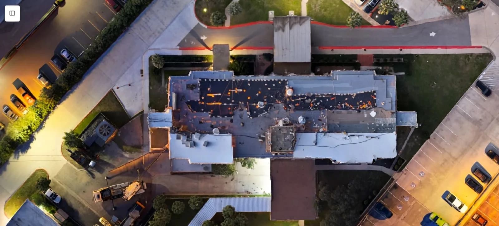 Aerial view of a large flat-roofed building with surrounding parking lots and roads at dusk