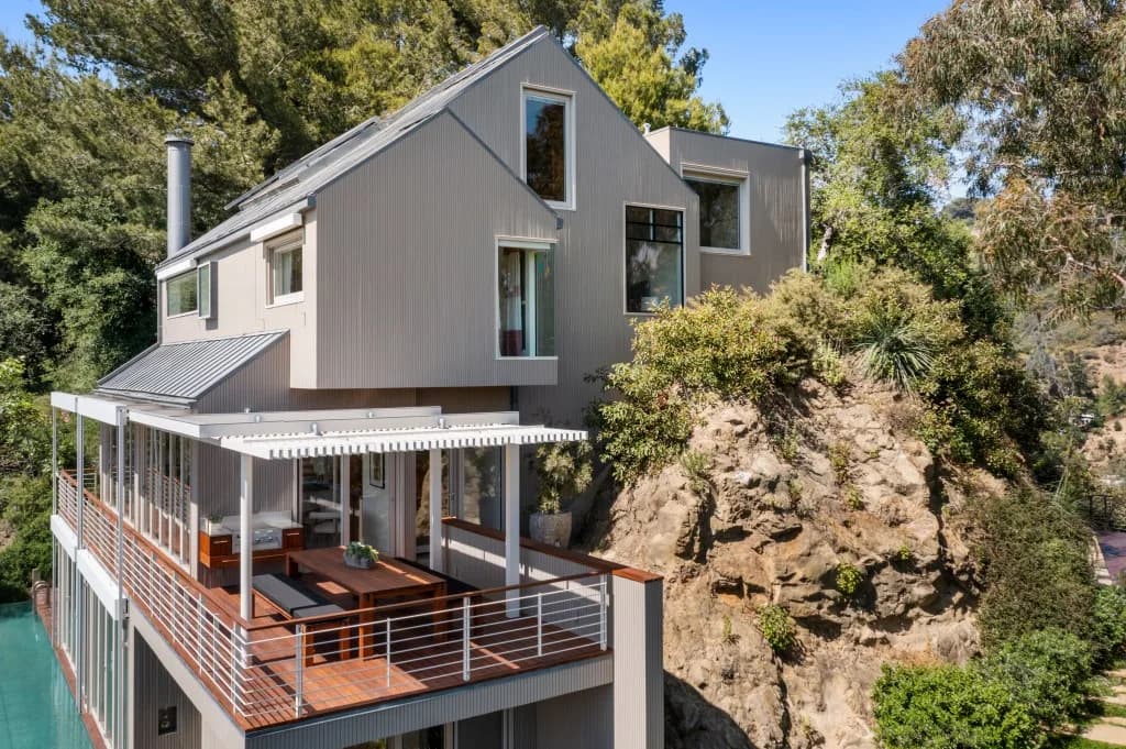 Modern hillside home with glass walls and a white pergola over a wooden deck