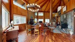 Wood-paneled living room with a dining table, chairs, chandelier, piano, and stone fireplace
