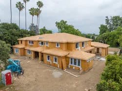 Two-story tan stucco building with multiple windows, portable toilet on left, and palm trees in background