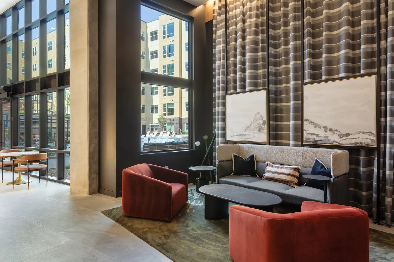 Lobby seating with large windows, striped curtains, gray sofa, red chairs, and framed landscape art