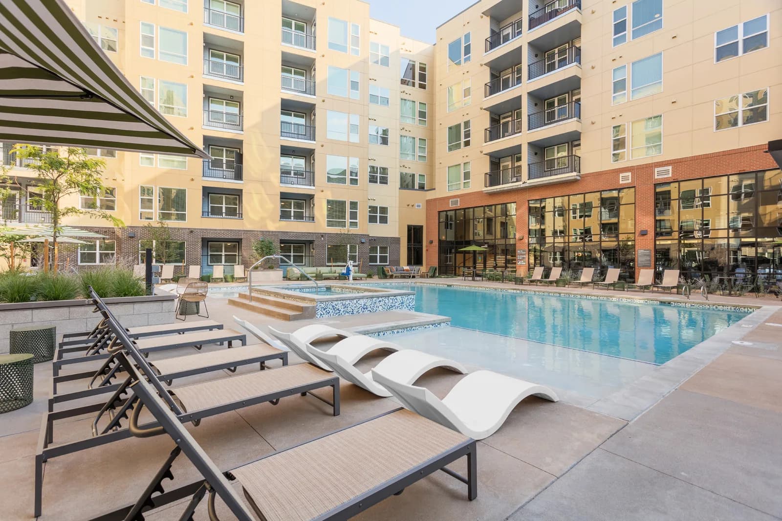 Pool in a modern apartment courtyard with sun loungers and a striped canopy