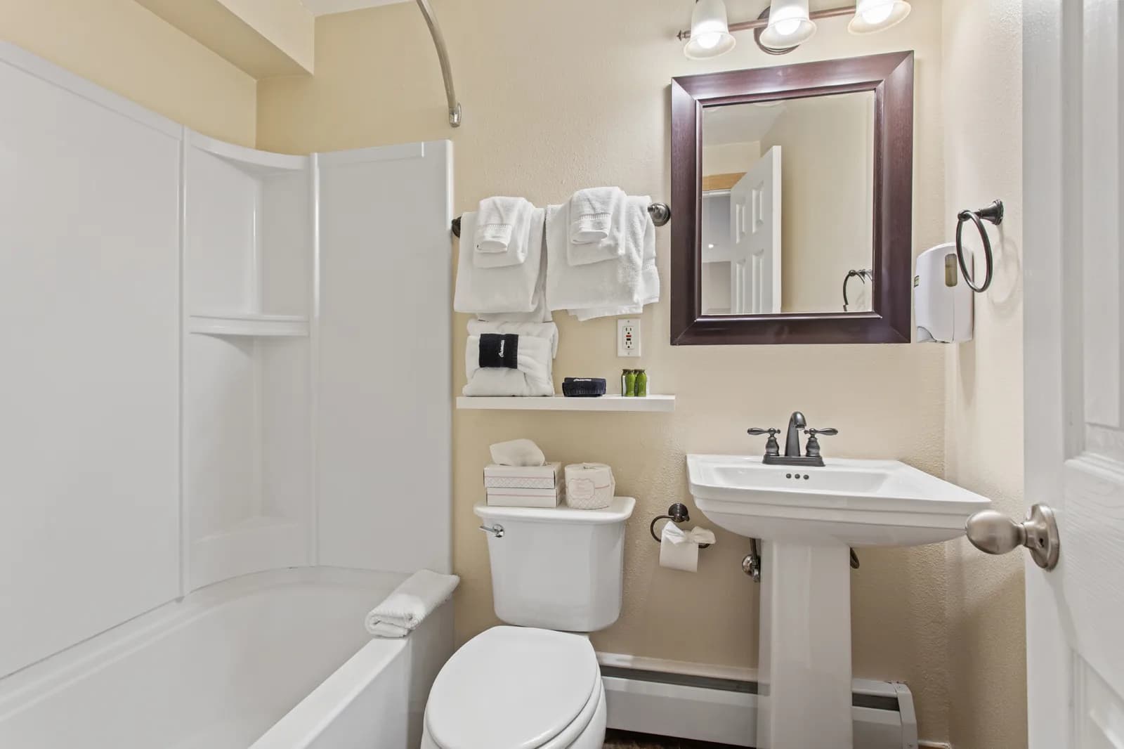Bathroom scene with white tub and curved shower, stacked towels, pedestal sink, dark framed mirror