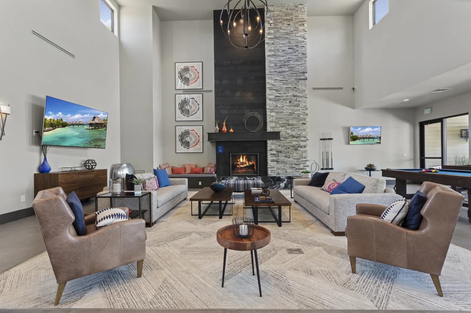 Spacious modern living room with a tall stone fireplace, two sofas, lounge chairs, art, and a pool table