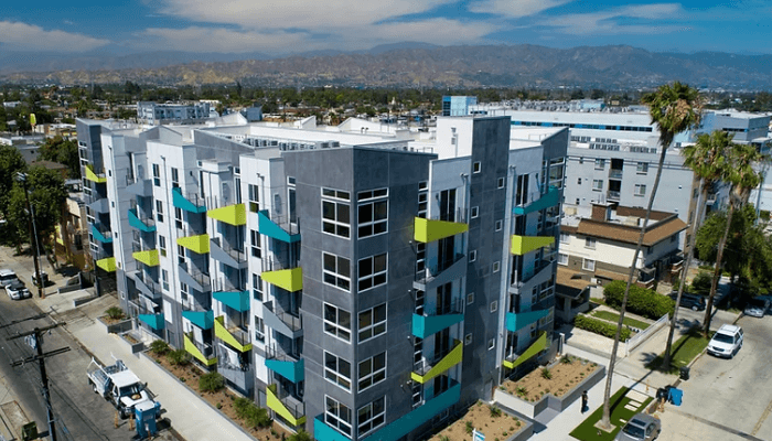 Aerial view of a modern grey apartment building with teal and lime balcony panels, streets and hills