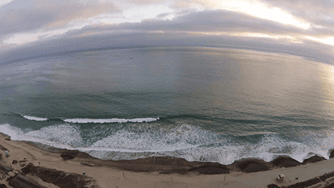 Aerial view of a sandy coastline with waves washing onto the shore and a cloudy sky