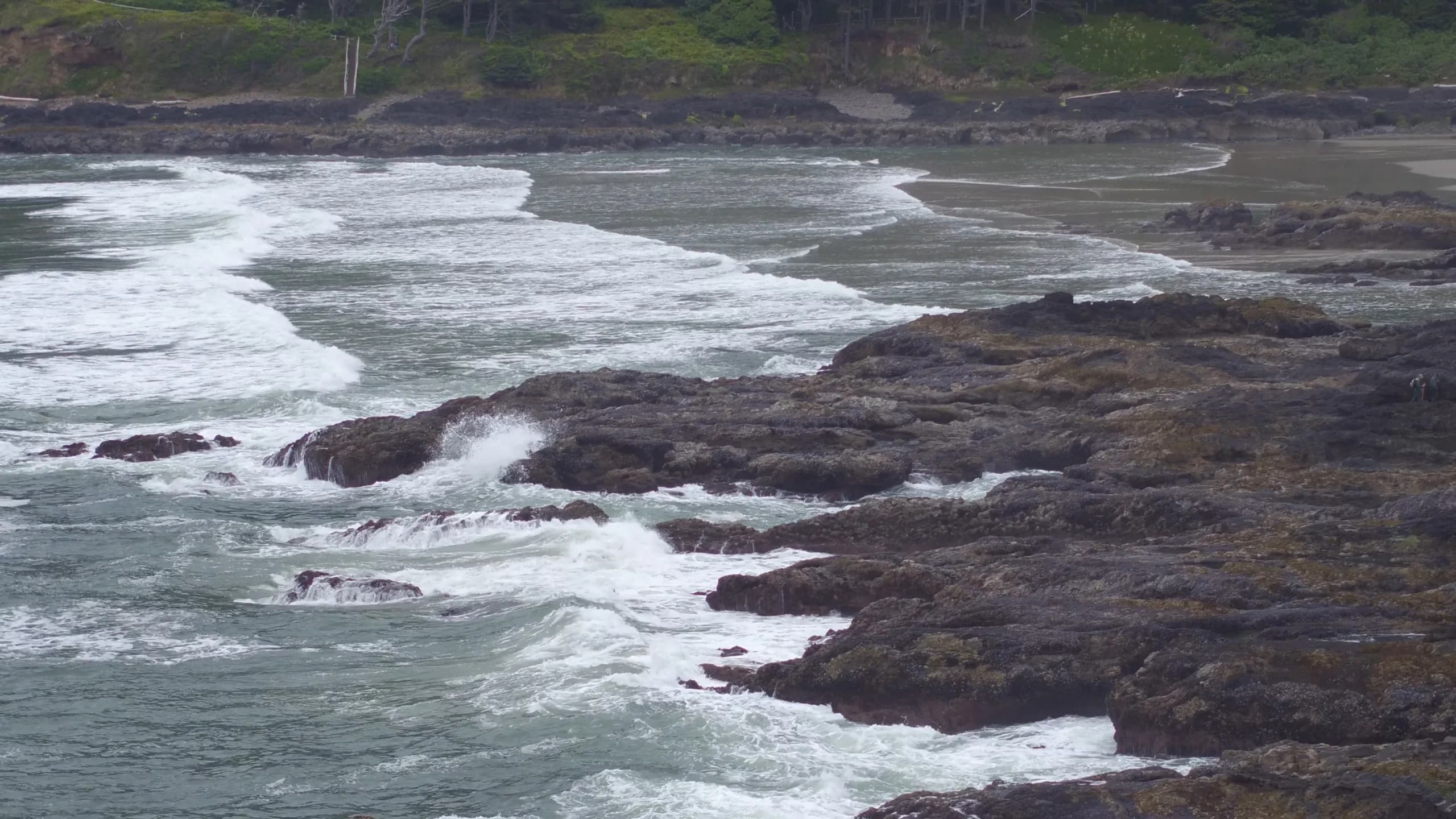 Aerial view of a rocky coastline with waves and a green hillside