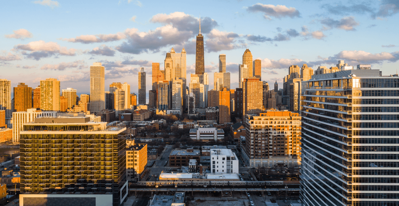 Aerial view of a city skyline at golden hour with tall glass buildings and a rail line in the foreground
