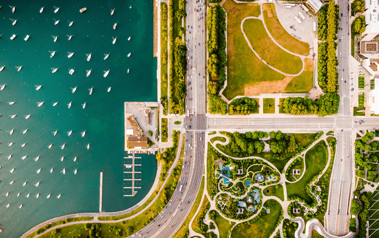 Aerial view of teal water with numerous boats, a marina, and a park with winding paths and roads